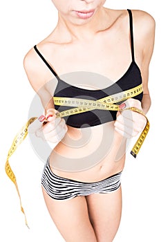 Young fit woman wearing black bra and panties, holding measuring tape with her hands on chest, isolated a white