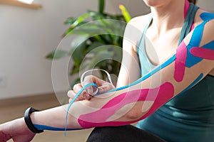 Young fit women applying elastic tape to her hand on a sunny day at home in attic. Kinesiology physical therapy