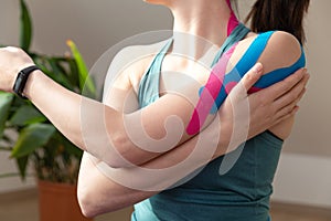 Young fit women wearing kinesio tape on her shoulder. Performing exercise at home. Kinesiology physical therapy