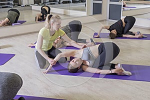 Young fit Women on a Yoga Pilates group class in gym. They stretch, stay in asana poses in sport outfit. Daylight. Indoors