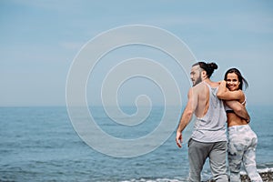 Young fitness couple embracing standing on beach, looking at horizon