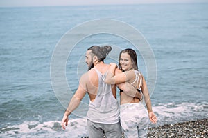 Young fitness couple embracing standing on beach, looking at horizon