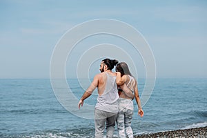 Young fitness couple embracing standing on beach, looking at horizon