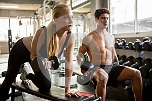 Young fitness couple lifting dumbbells together at  gym in morning light .  bodybuilder man and woman showing muscle . two people