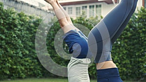 Young fitness couple practicing headstand yoga pose outside in garden of house. Asian woman and Caucasian man working