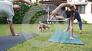 Young fitness couple practicing yoga with pet dog outside in garden of house. Asian woman and Caucasian man training