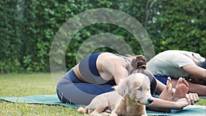 Young fitness couple practicing yoga with their pet dog outside in garden of house. Asian woman and Caucasian man