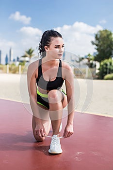 Young fitness girl tying shoelaces on the beach