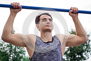 Young fitness man lifts up on horizontal bar during workout