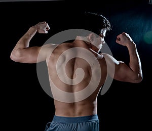 Young fitness muscly man showing his back,shoulders, triceps and biceps muscles after training