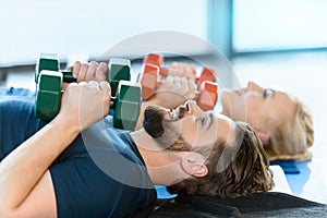 Young fitness people exercising with dumbbells at fitness studio