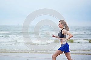 Young fitness running woman jogging on beach