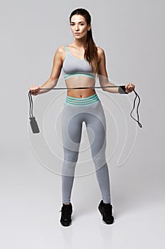 Young fitness sportive girl posing looking at camera holding jumping rope over white background.