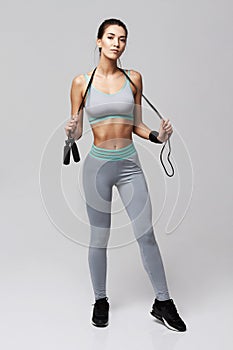 Young fitness sportive girl posing looking at camera holding jumping rope over white background.