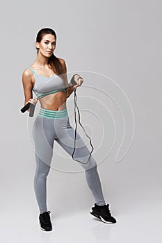 Young fitness sportive girl posing looking at camera holding jumping rope over white background.
