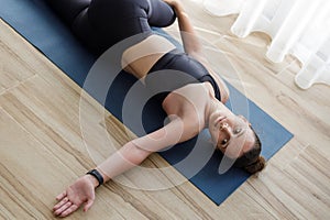 Young fitness woman in black sportswear doing twist stretching of her spine