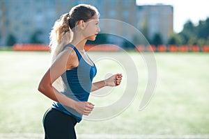 Young fitness woman in a blue shirt and leggings running on a stadium track. Athlete girl doing exercises on the training at stadi