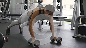 Young fitness woman doing dumbbell rows at crossfit gym. Sportive girl exercising - pulls weight. Beautiful female