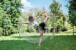 Young fitness woman doing practicing yoga or pilates exercise on green grass at park