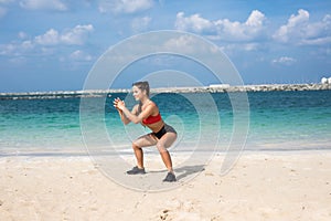 Young fitness woman doing squat exercises against sea