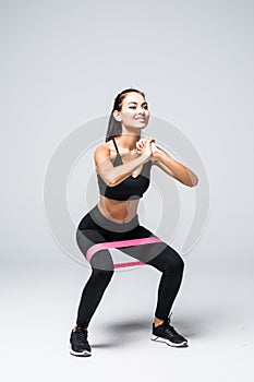 Young fitness woman doing squats with fitness loop band isolated on white background