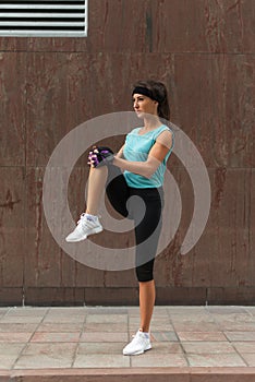 Young fitness woman doing warm-up exercise before running stretching her leg by performing knee to chest stretch on the