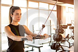 Young fitness woman execute exercise on cable machine in gym