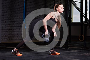 Young fitness woman exercising cross fit with kettlebell against brick wall in the gym.