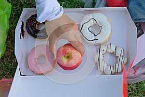 Young fitness woman holding in hands red apple and donut