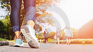 Young fitness woman legs walking with group of people exercise walking in the city public park in morning