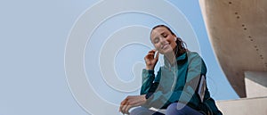 Young fitness woman listening to music while resting after workout session on sunny morning.