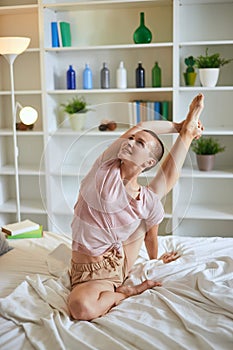 Young fitness woman in pajamas doing exercises at home on bed. Healthy lifestyle