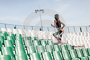 Young Fitness woman with a sports figure in leggings and black top running up on stone stairs at the stadium with sun spot