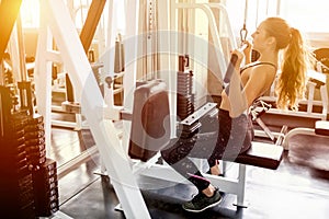 young fitness woman in sportswear exercising building muscles with machine Cable Crossover in sport gym morning ligth.workout