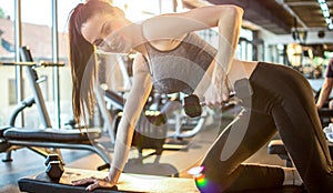 Young fitness woman in sportswear working out with weights over exercise bench in gym.