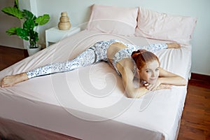 Young fitness woman in sportwear practicing yoga on bed in bedroom at home in Morning . sport girl lying down and stretching legs