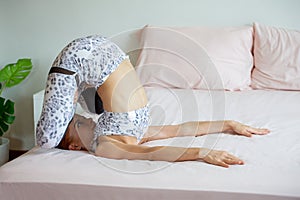 Young fitness woman in sportwear practicing yoga on bed in bedroom at home in Morning . sport girl stretching legs, arm, body