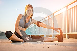 Young fitness woman stretching muscles before sport activity on bridge sidewalk during sunset.