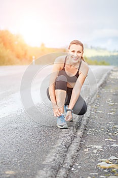 Young fitness woman tying her shoes before jogging