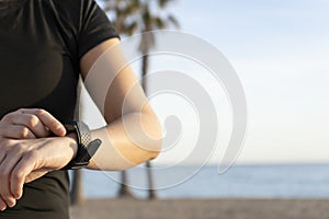 Young fitness woman using smart watch before or after running on beach background with palm trees.Sports wellness and athletics