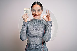 Young fitness woman wearing sport workout clothes holding paper with diet word doing ok sign with fingers, excellent symbol