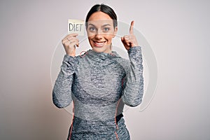 Young fitness woman wearing sport workout clothes holding paper with diet word surprised with an idea or question pointing finger