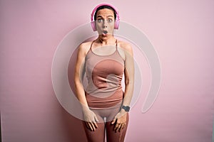 Young fitness woman wearing sport workout clothes wearing headphones listening to music afraid and shocked with surprise