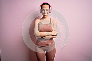 Young fitness woman wearing sport workout clothes wearing headphones listening to music happy face smiling with crossed arms