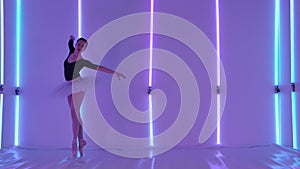 Young flexible ballerina in a white ballet tutu and pointe shoes in the studio against the background of neon tubes. The