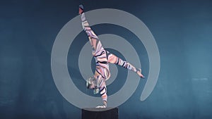 Young flexible blonde circus acrobat posing in studio in costume. Doing equilibre balance handstand on a cube.
