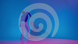 Young flexible energetic man dancing contemp experimental dance in bright sportive clothes on blue background at dance