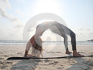 Young flexible girl practice wheel yoga pose at seaside at sunset