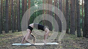 young flexible slim female practices yoga, performs bridge pose at pine forest