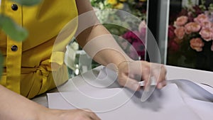 Young florist cutting wrapping paper for bouquet at workplace. Floral artist working in flower shop studio. Floristry